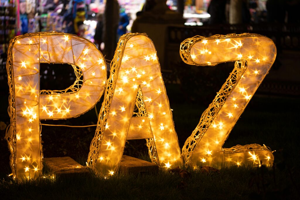 pexels-photo-20777342-20777342 Glowing 'PAZ' sign with warm lights against a blurred urban background at night.
